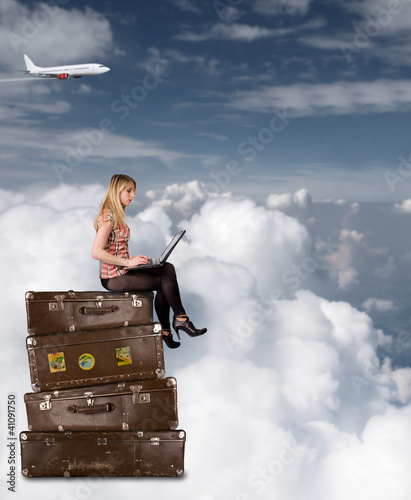 Photo: Beautiful blond girl sitting on suitcases above clouds Beautiful blond girl sitting on suitcases above clouds