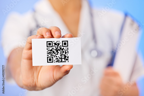 Photo: Doctor holding business card with health care QR code on blue Doctor holding business card with health care QR code on blue