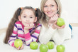 Young mom and her daughter lying on the floor with green apples