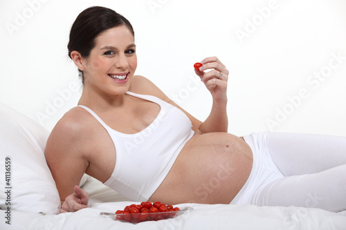 Photo: A pregnant woman eating strawberries on her bed. A pregnant woman eating strawberries on her bed.