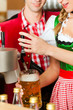 Junge Frau in Tracht zapft ein Bier im Restaurant