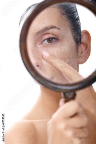 Photo: Young woman examining skin with magnifier Young woman examining skin with magnifier