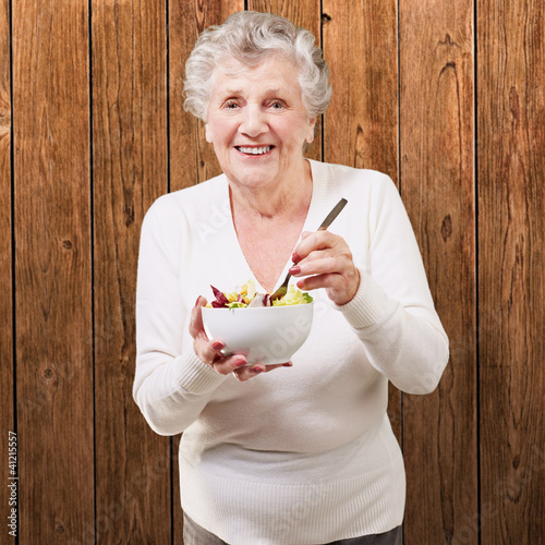 Foto: portrait of senior woman eating salad against a wooden wall portrait of senior woman eating salad against a wooden wall