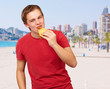 portrait of young man eating pizza against a beach