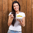 portrait of healthy woman eating salad against a wooden wall