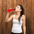 portrait of young sporty woman drinking isotonic drink against a portrait of young sporty woman drinking isotonic drink against a
