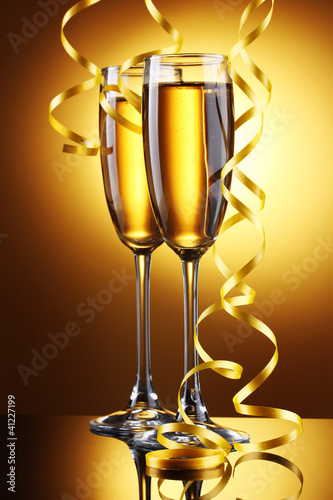 Photo: glasses of champagne and streamer on yellow background glasses of champagne and streamer on yellow background