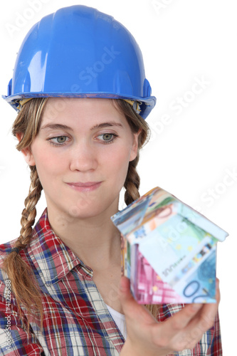 Photo: Female builder holding house made from bank notes Female builder holding house made from bank notes