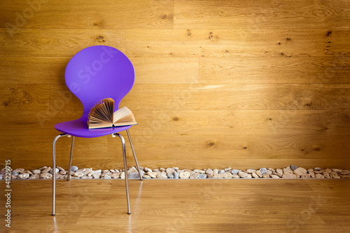 Foto: Purple chair with opened book next wooden wall / modern interior Purple chair with opened book next wooden wall / modern interior