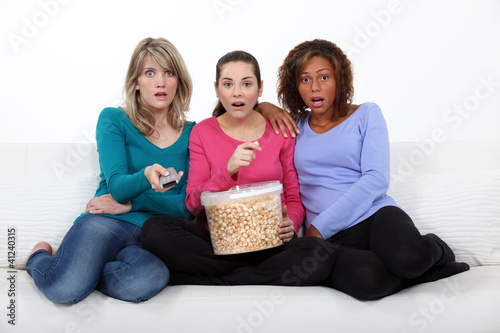 Photo: Three scared women sat on sofa watching movie Three scared women sat on sofa watching movie