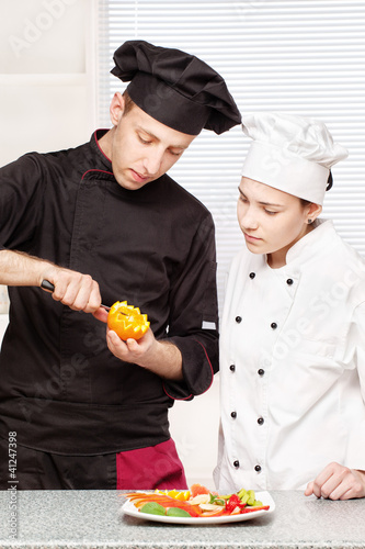 Foto: Senior chef teaches young chef to decorate fruit Senior chef teaches young chef to decorate fruit