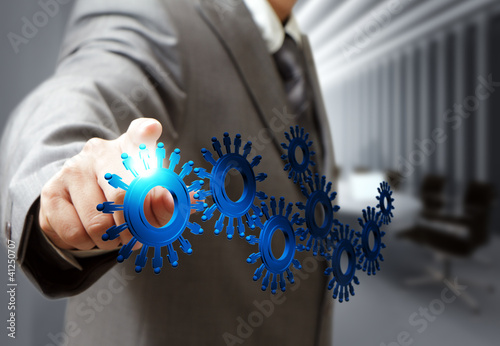 Photo: business man hand point cogs icons in board room business man hand point cogs icons in board room
