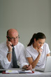 A grumpy businessman sitting beside his assistant
