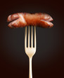 Grilled sausage on a fork on black background
