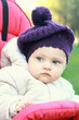 Funny baby girl in hat outdoor sit in stroller and looking. Clos Funny baby girl in hat outdoor sit in stroller and looking. Clos