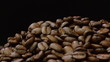 A pile of roasted coffee beans rotating on black background.