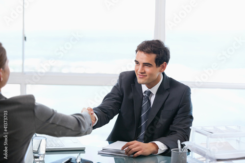 Foto: Businessman shaking hands with a client while sitting Businessman shaking hands with a client while sitting