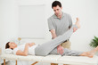Brunette physiotherapist raising the leg of a patient