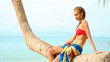Sexy woman in bikini sitting on a palm tree at the beach