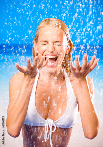 Photo: Young woman at rain or summer shower on beach Young woman at rain or summer shower on beach