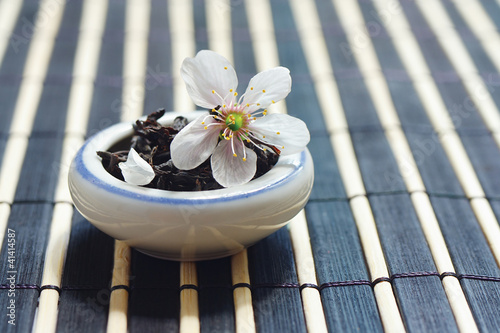 Photo: Jar of tea leaves and cherry blossoms on bamboo table cloth Jar of tea leaves and cherry blossoms on bamboo table cloth