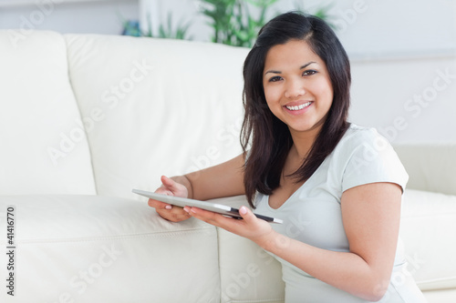 Photo: Smiling woman holding a tactile tablet in front of a sofa Smiling woman holding a tactile tablet in front of a sofa