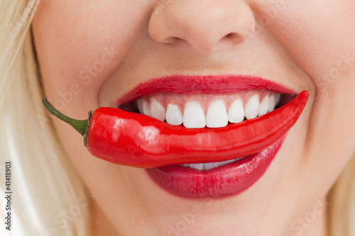 Foto: Happy blonde woman holding a chili with her mouth Happy blonde woman holding a chili with her mouth