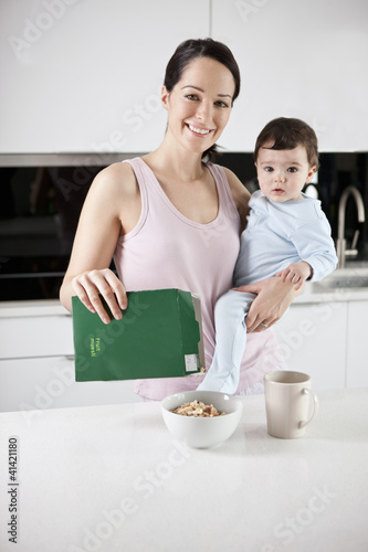 Photo: A young mother holding her baby son whilst making breakfast A young mother holding her baby son whilst making breakfast
