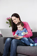 A mother and baby sitting on a sofa looking at a laptop