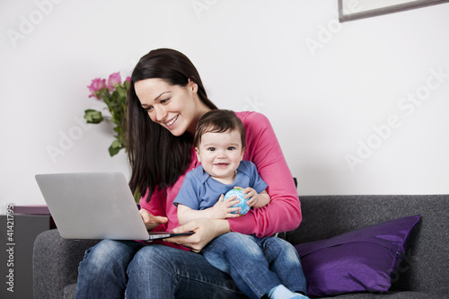 Photo: A mother using a laptop whilst holding her baby son on her lap A mother using a laptop whilst holding her baby son on her lap