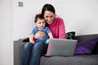 A mother and her baby son sitting on a sofa looking at a laptop