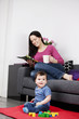 A mother relaxing on a sofa with a magazine, baby playing