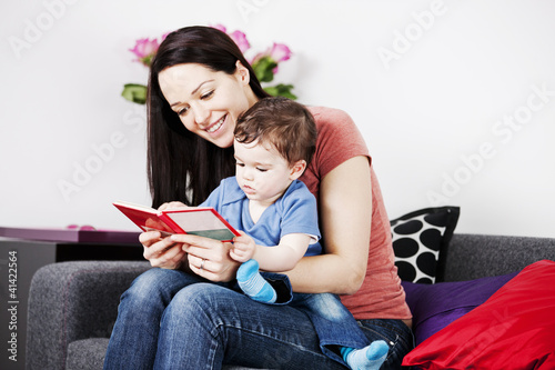 Photo: A mother and her baby son sitting on the sofa reading a book A mother and her baby son sitting on the sofa reading a book