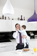 A father trying to use the telephone whilst holding his baby son