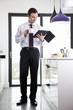 A businessman standing in a kitchen holding a digital tablet