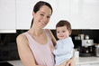A young mother standing in a kitchen holding her baby son