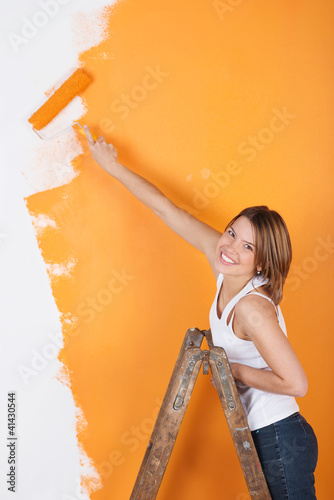 Foto: lächelnde frau streicht eine wand orange lächelnde frau streicht eine wand orange