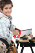 Young boy dressed as an adult carpenter cutting wood with a saw