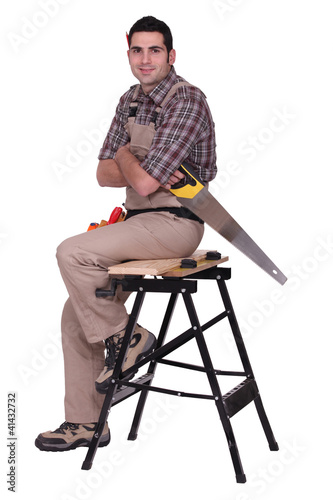 Photo: Laborer with saw sitting on a workbench Laborer with saw sitting on a workbench