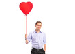 Photo: A smiling young male holding a red heart shaped balloon A smiling young male holding a red heart shaped balloon