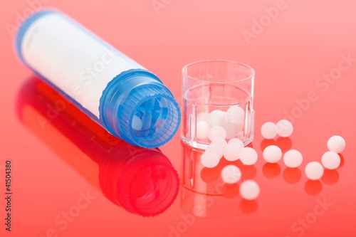 Photo: Homeopathic pills and container on red Homeopathic pills and container on red
