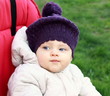Funny baby in hat outdoot sitting in red bright stroller on gree Funny baby in hat outdoot sitting in red bright stroller on gree