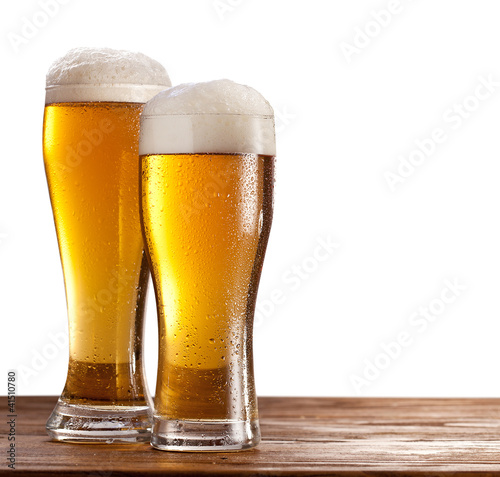 Photo: Two glasses of beers on a wooden table. Two glasses of beers on a wooden table.