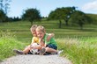 Zwei Kinder mit Fußball sitzen auf einem Feldweg