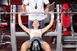 fitness woman lifting barbell in gym with trainer's help