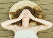 Woman lying on deck, wrapped in towel, head on mat, hands over eyes