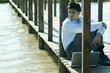 Businessman on wooden footbridge over lake with laptop, looking away