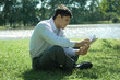 Businessman sitting on grass, reading