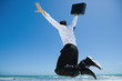 Businessman on beach, jumping into air with briefcase in hand