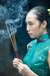Foto: Young woman wearing traditional Chinese clothing, holding up incense, side view Young woman wearing traditional Chinese clothing, holding up incense, side view